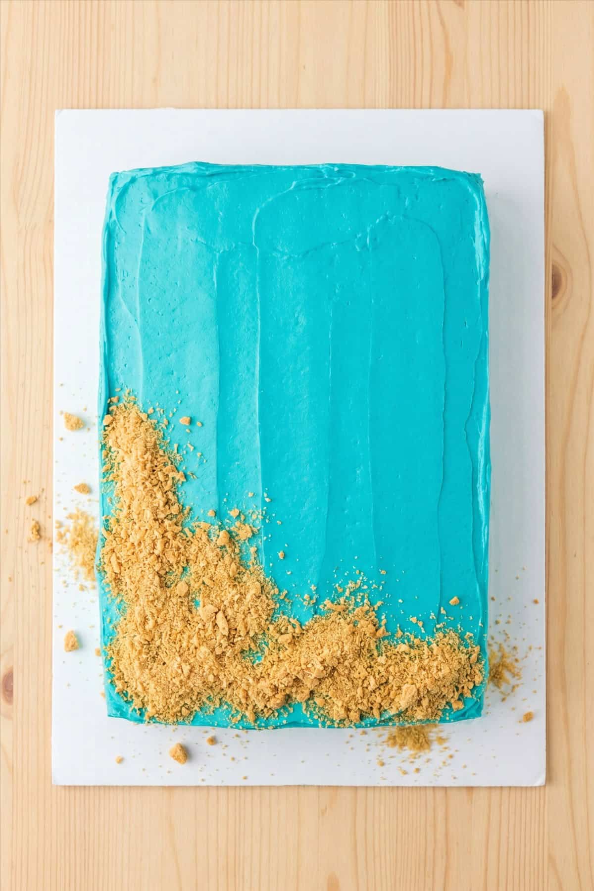 A sheet cake frosted with turquoise blue buttercream and graham cracker sand.