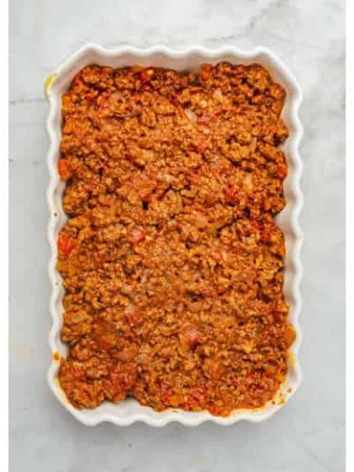 Spiced meat sauce spread over the eggplant layer in a baking dish.