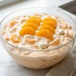 A glass bowl of creamy mandarin orange fluff salad topped with mandarin orange segments.
