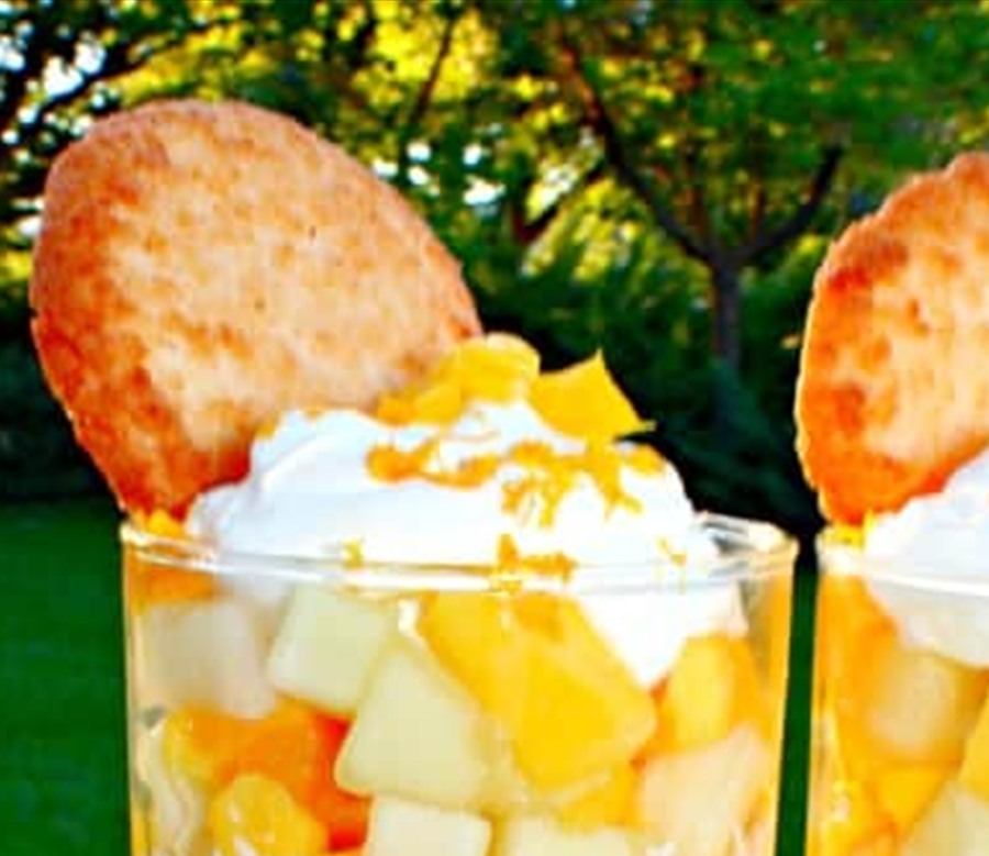 A mango dessert verrine topped with whipped cream, orange zest, and a crisp cookie ready to serve.