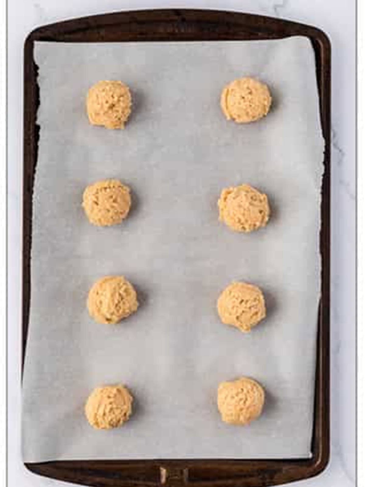 Cookie dough balls scooped onto a parchment lined baking sheet.