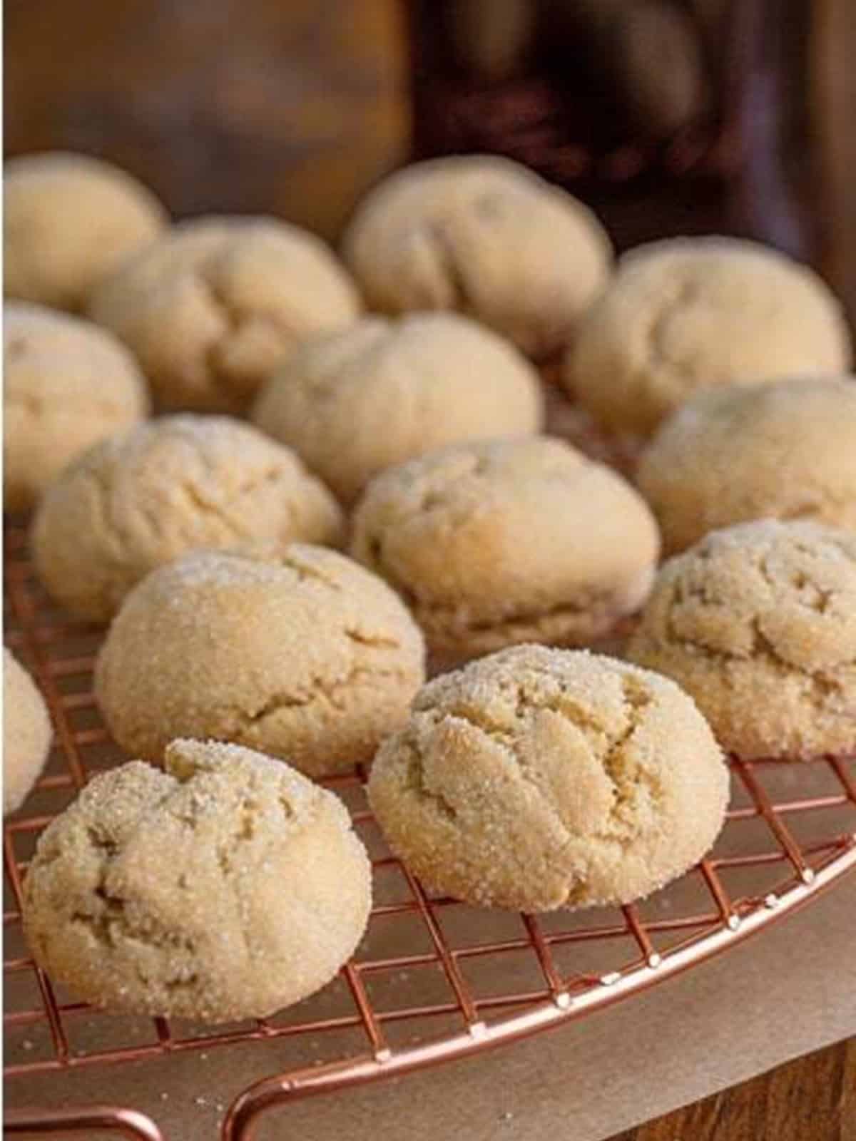 Baked maple cookies cooling on a copper wire rack with crackled sugar tops.
