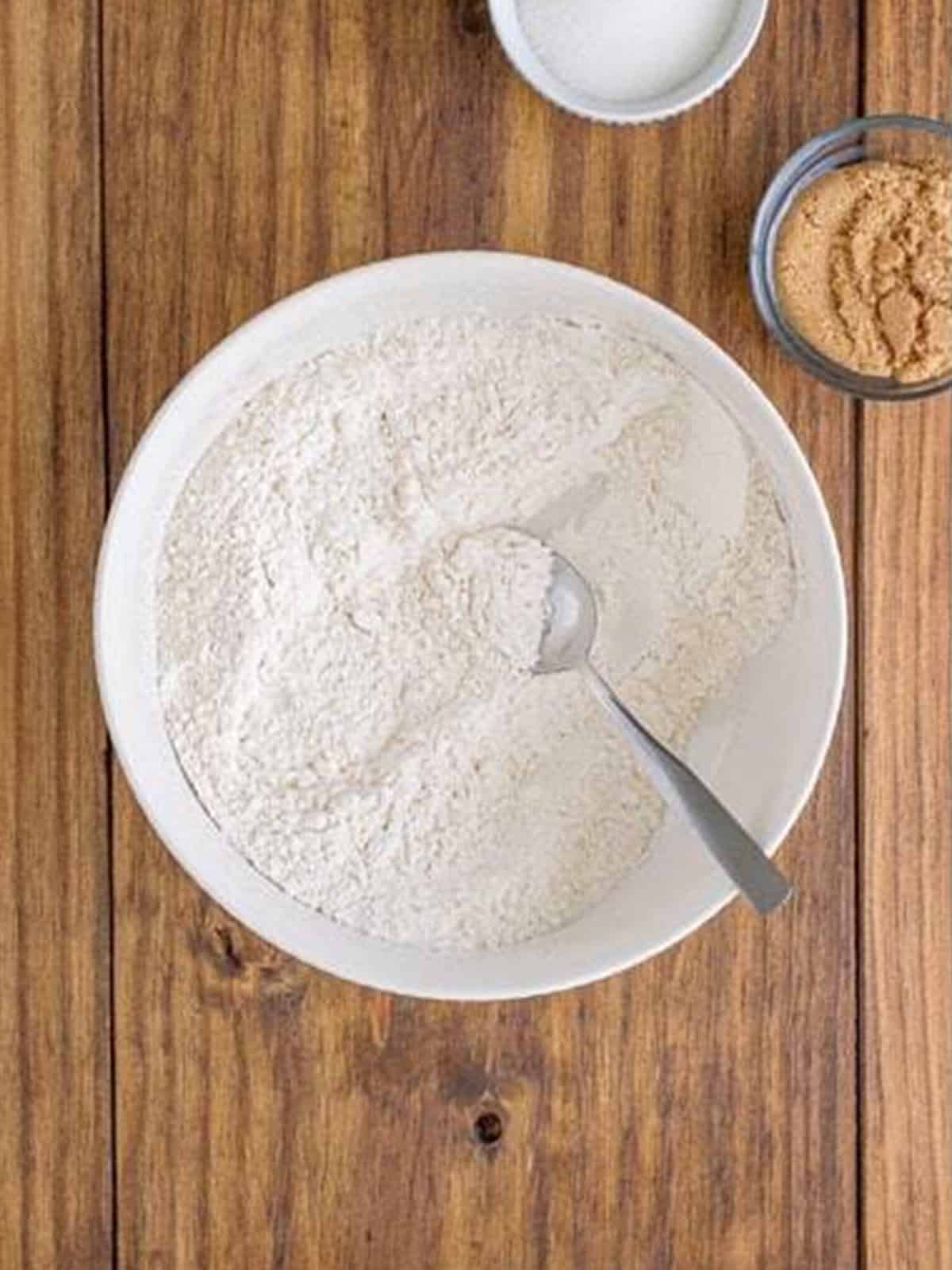 Flour, cornstarch, baking soda, salt, and baking powder whisked together in a white bowl for maple cookies.