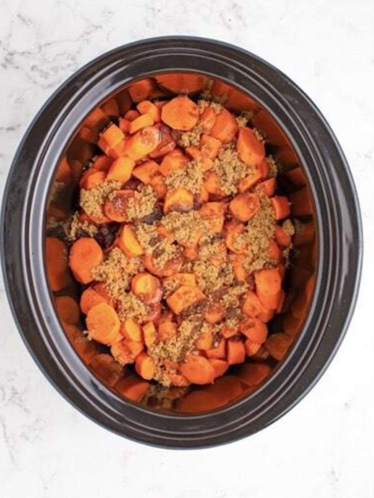 Sliced carrots topped with brown sugar in a slow cooker.