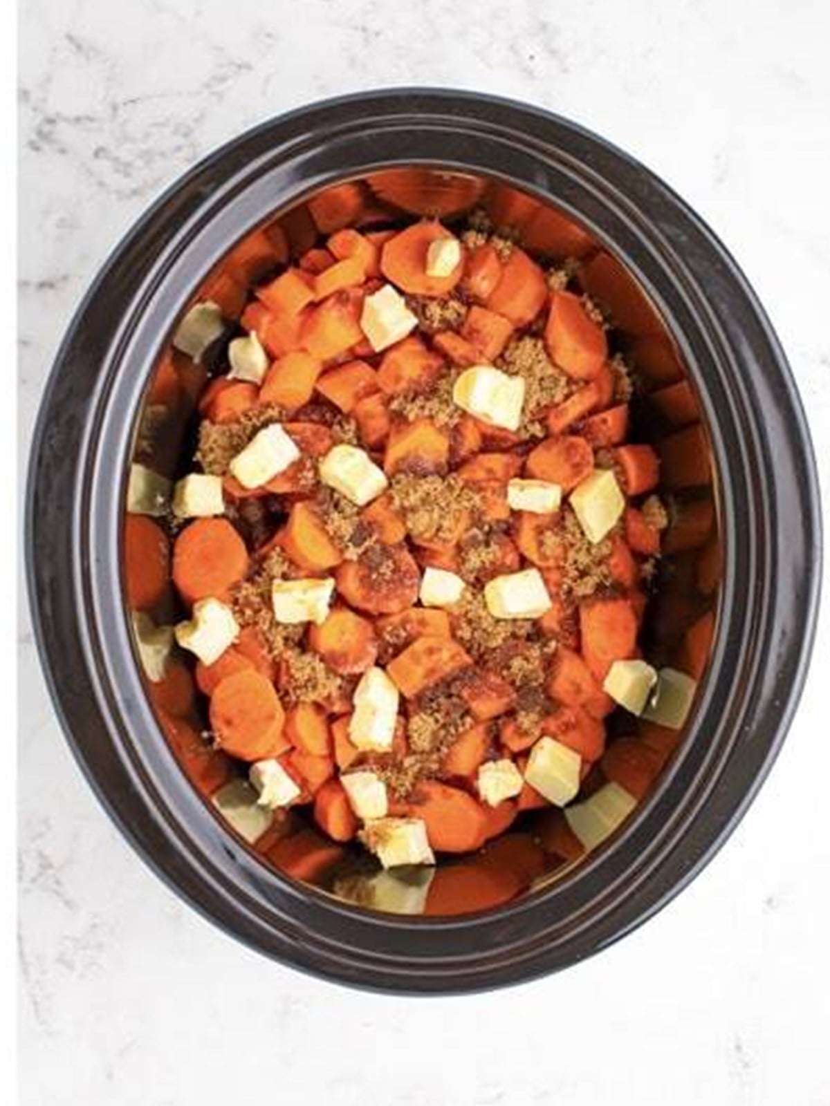 Carrots with maple syrup, salt, and pats of butter in a slow cooker.