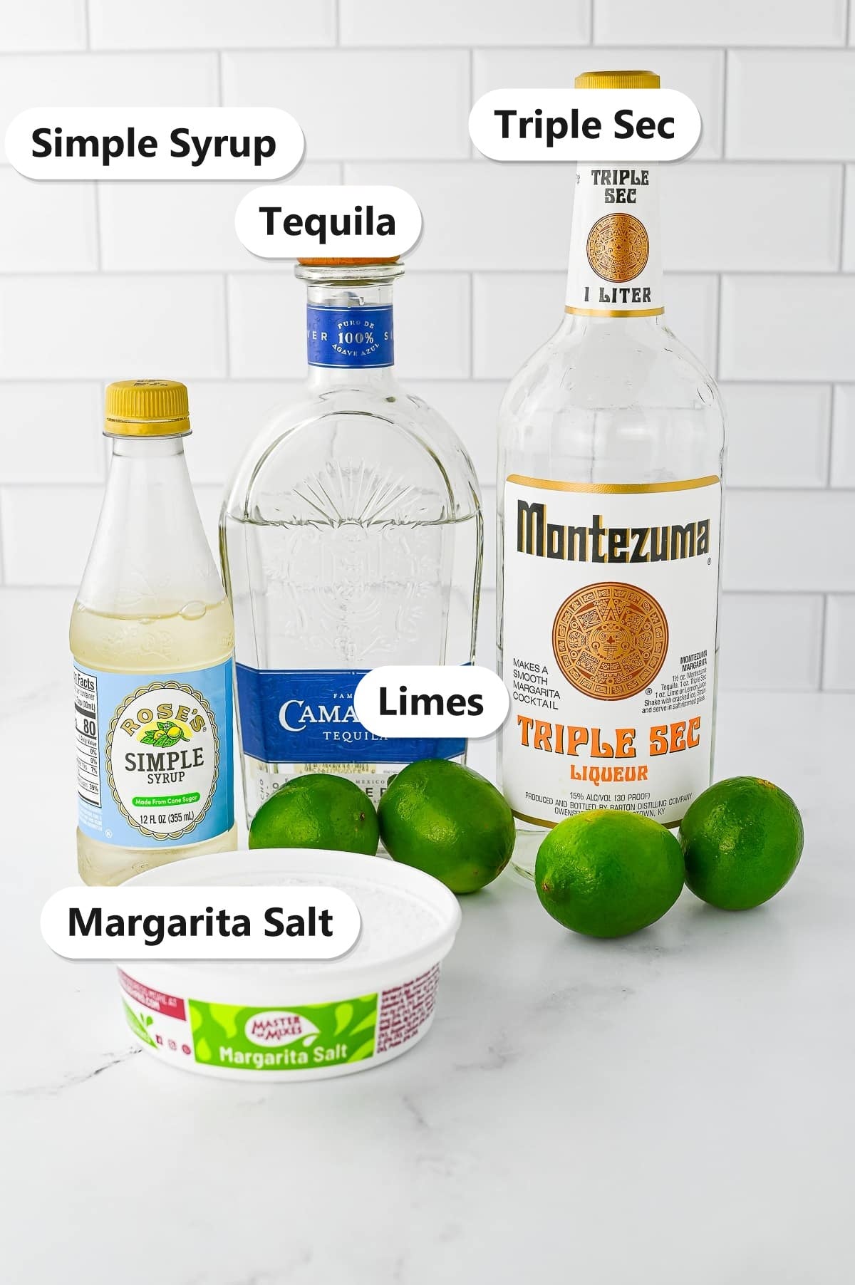 Labeled ingredients for a margarita including tequila, triple sec, simple syrup, fresh limes, and margarita salt.
