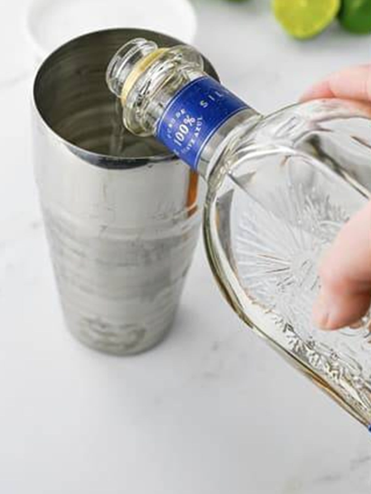 Tequila being poured into a cocktail shaker filled with ice.