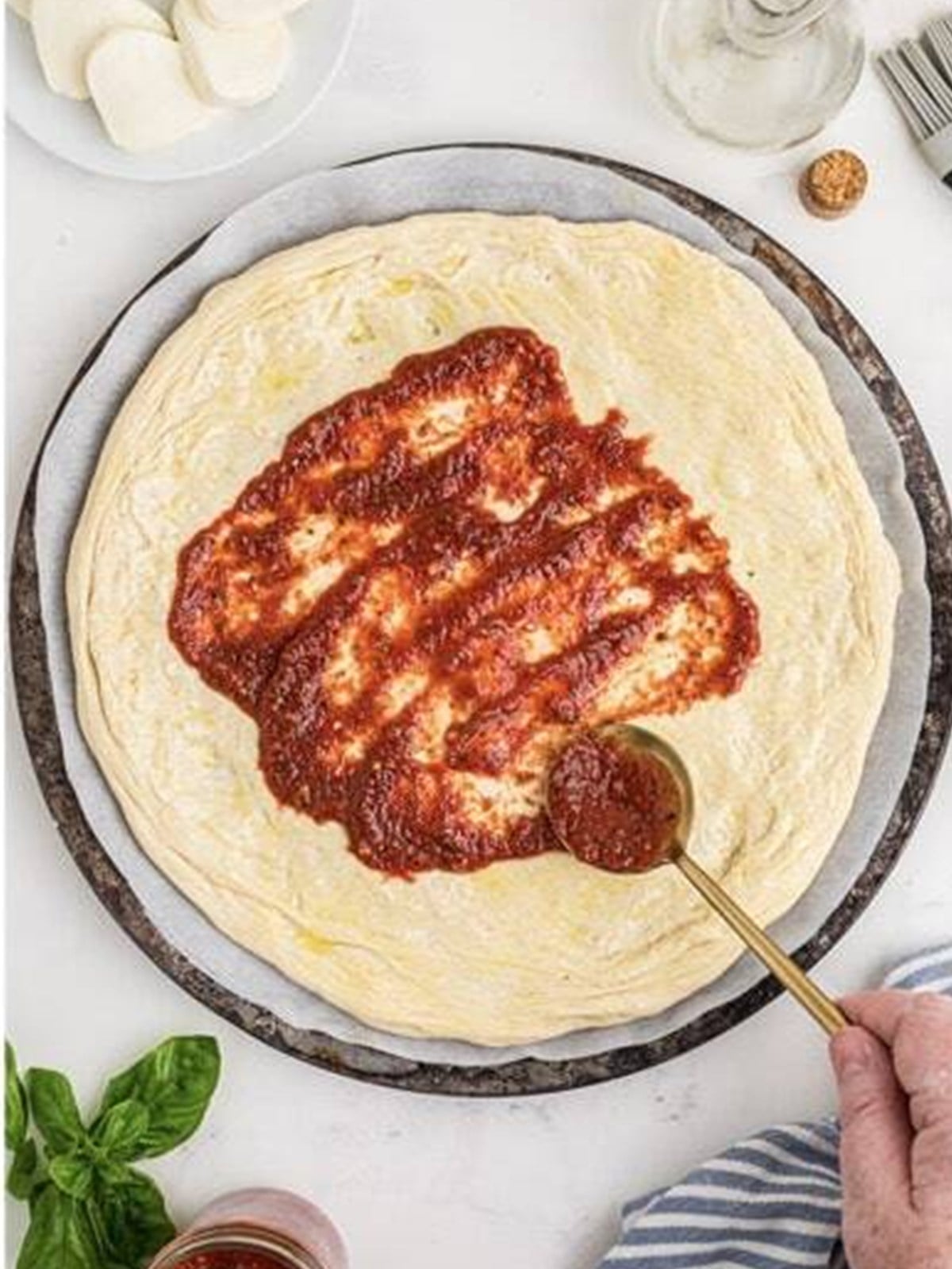 Spreading a thin layer of pizza sauce over the dough