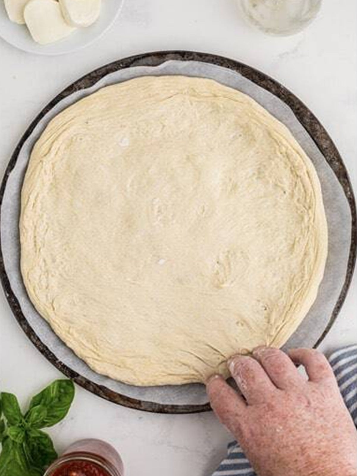 Stretching pizza dough on a parchment-lined pizza tray