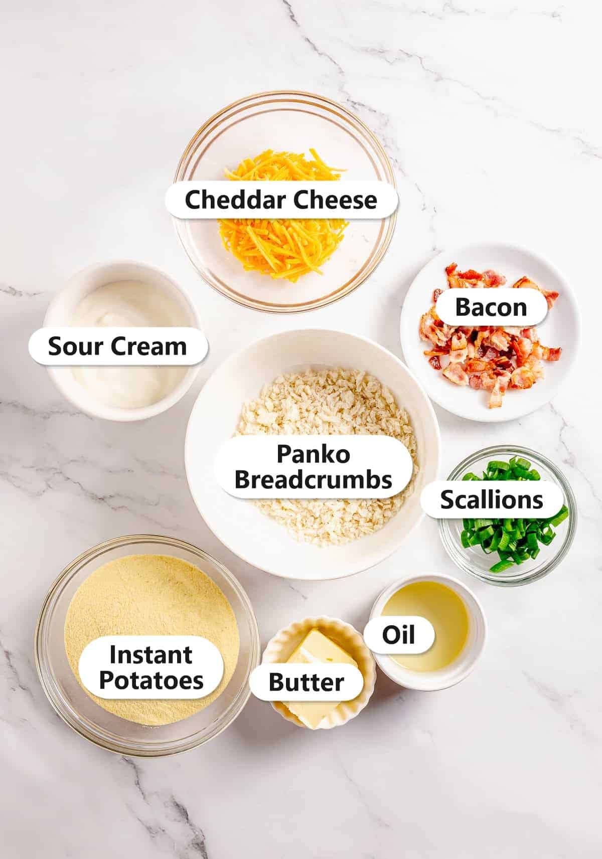 Labeled mashed potato cakes ingredients including instant potatoes, cheddar cheese, bacon, scallions, panko breadcrumbs, sour cream, butter, and oil.