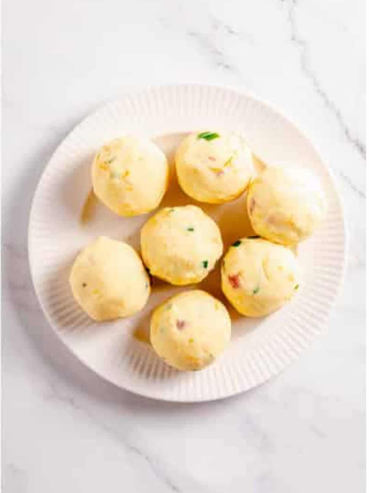 Loaded mashed potato mixture rolled into balls on a white plate.