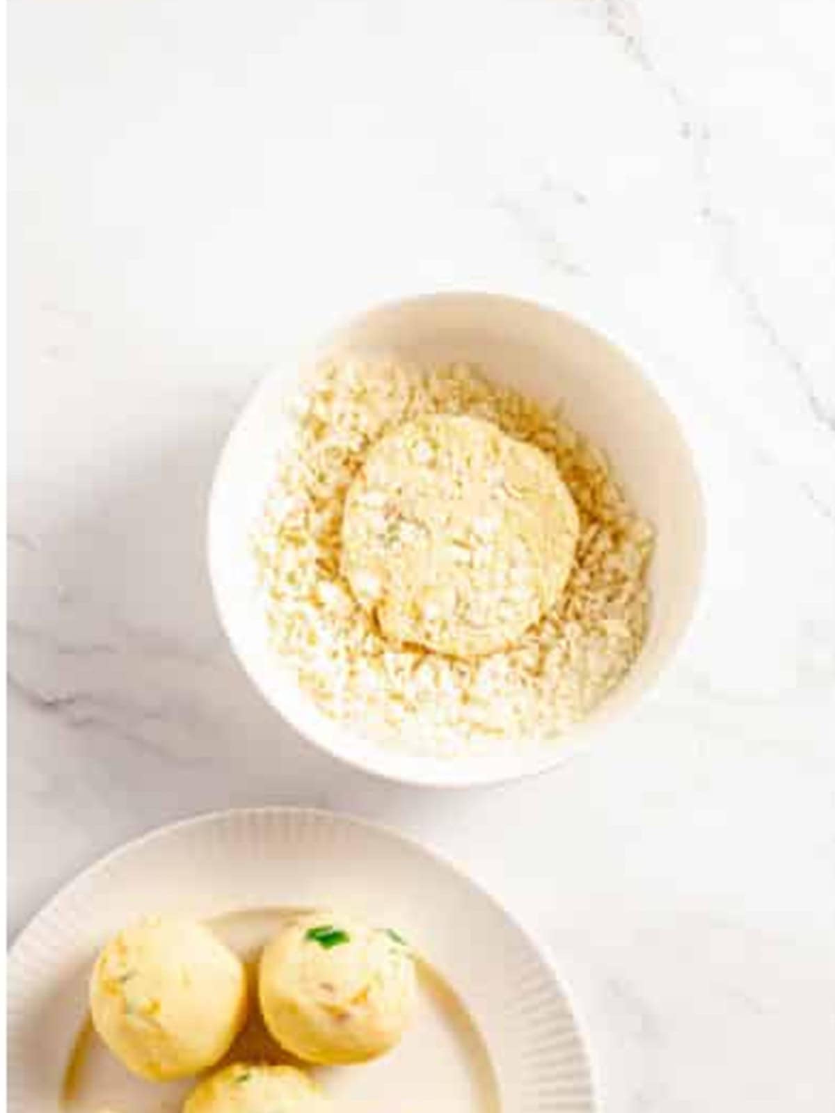 A mashed potato cake pressed into a bowl of panko breadcrumbs.