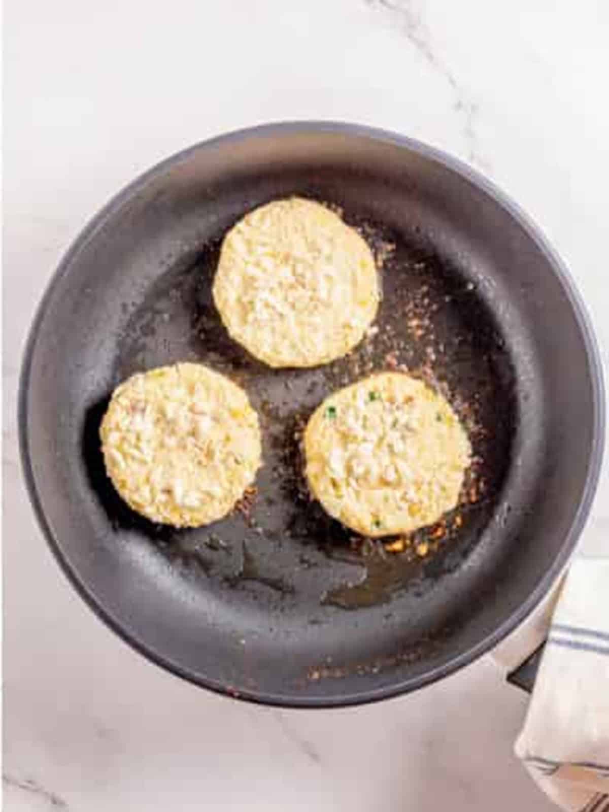 Mashed potato cakes pan frying in a skillet until golden brown.