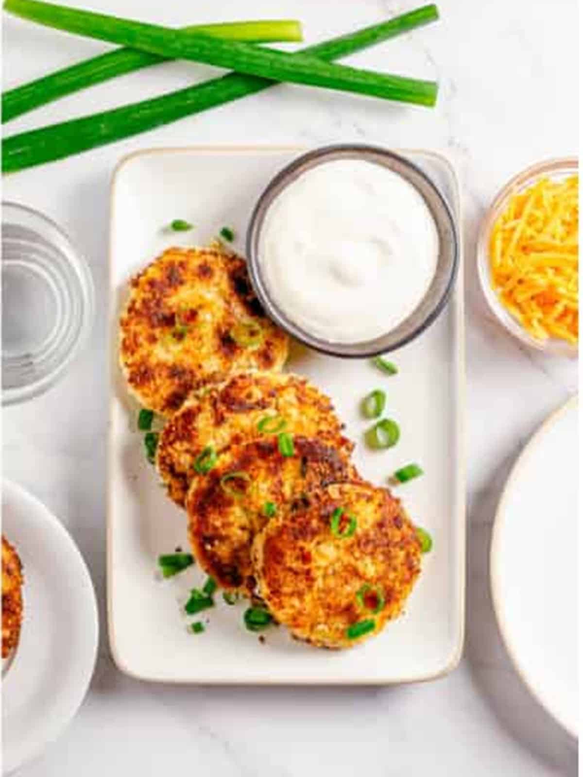Golden mashed potato cakes plated with sour cream and scallions.