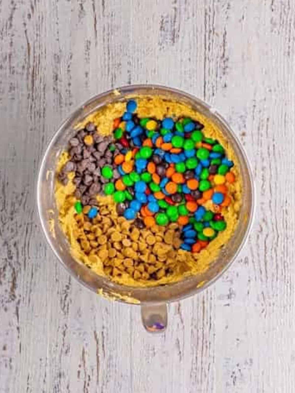 M and Ms, chocolate chips, and peanut butter chips stirred into monster cookie dough.