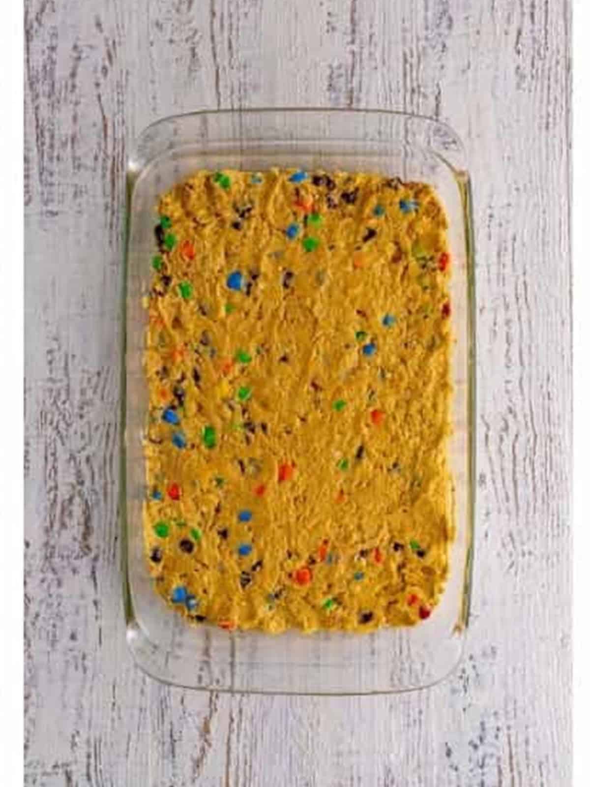 Monster cookie dough pressed into a baking dish topped with M and Ms.