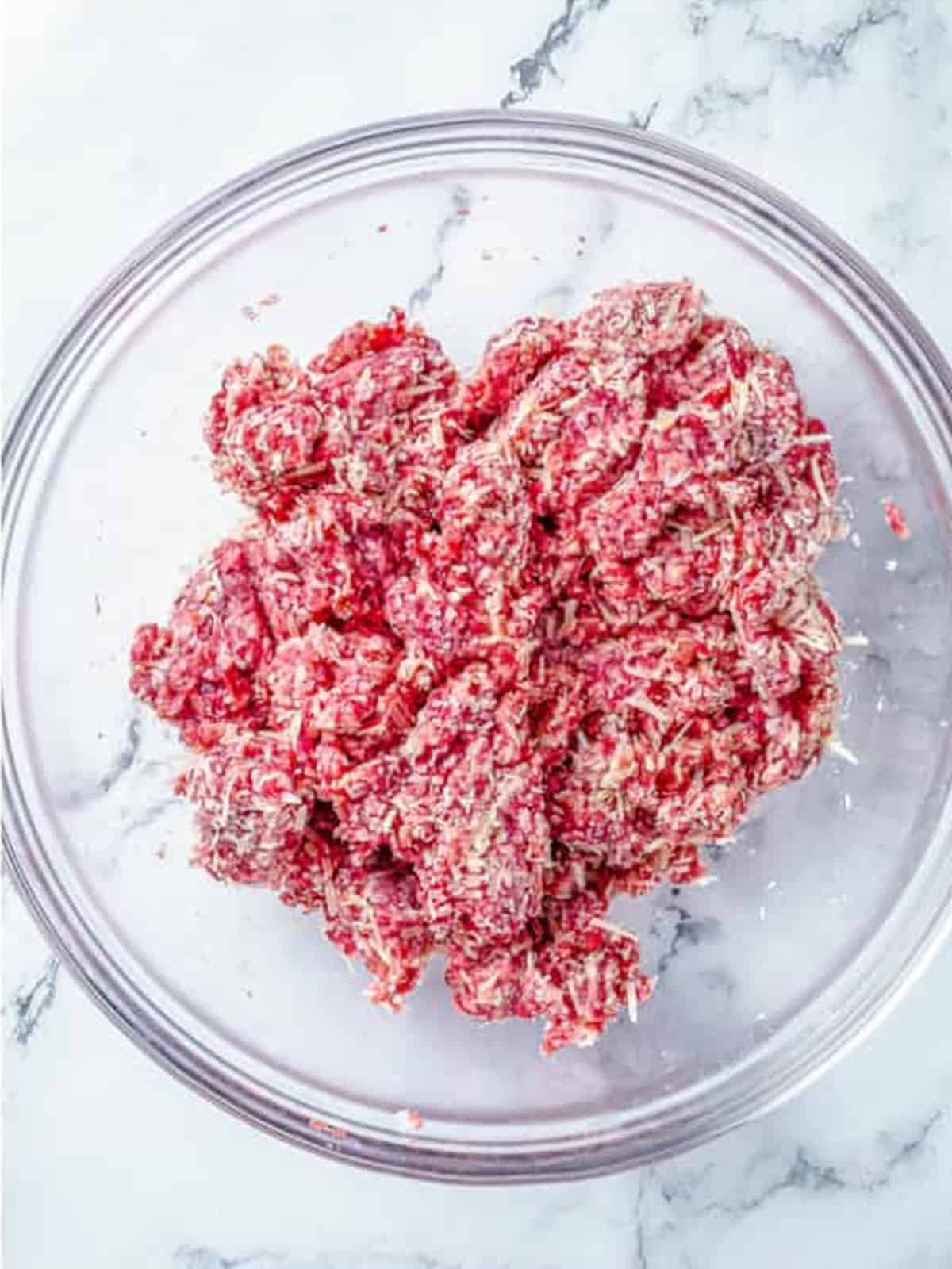 Raw ground beef in a glass bowl ready to brown for meat sauce.
