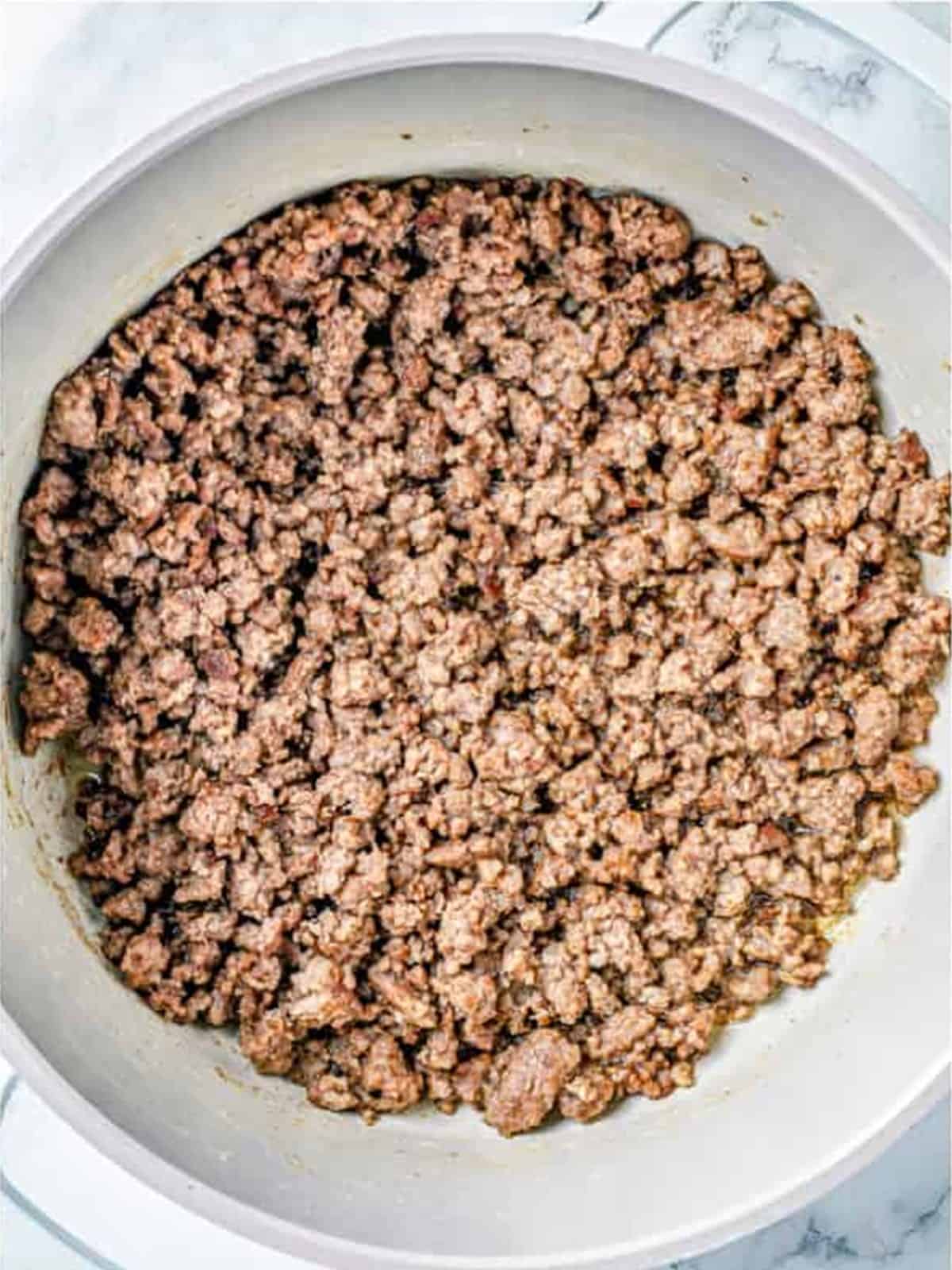 Ground beef browned in a large white pot for meat sauce.