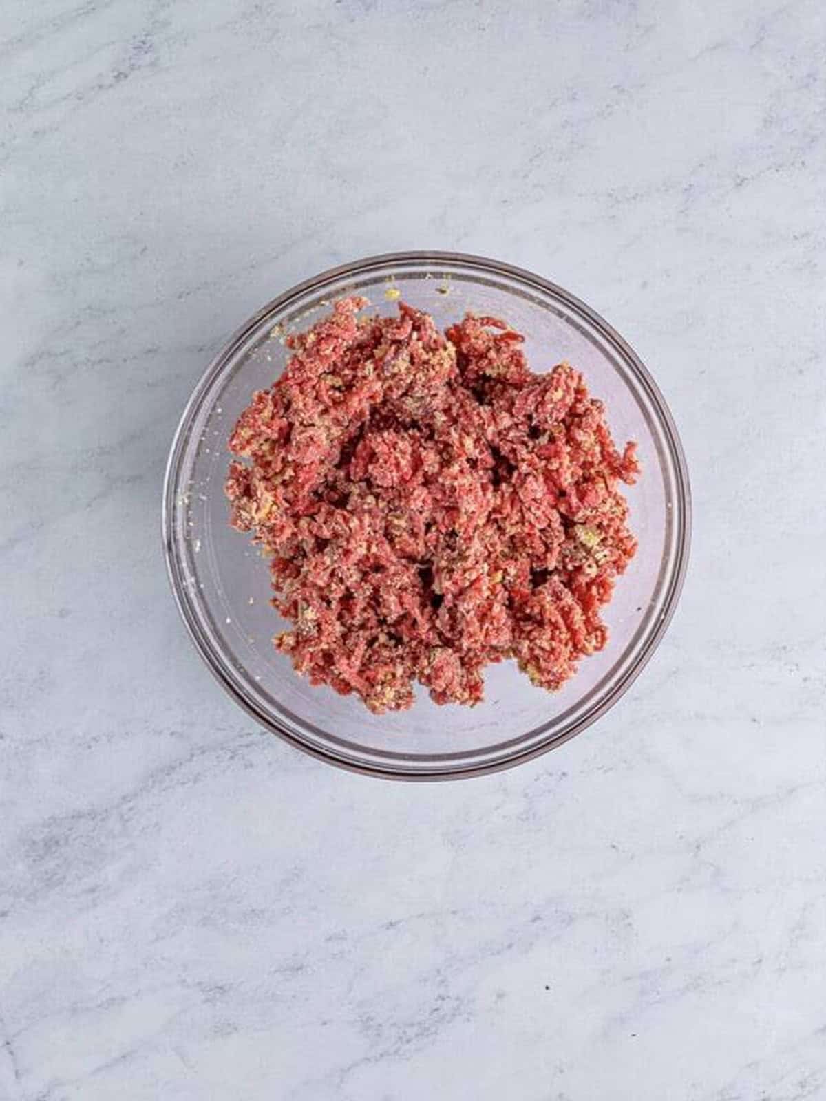 Ground beef mixed with parmesan, breadcrumbs, and seasonings in a bowl.