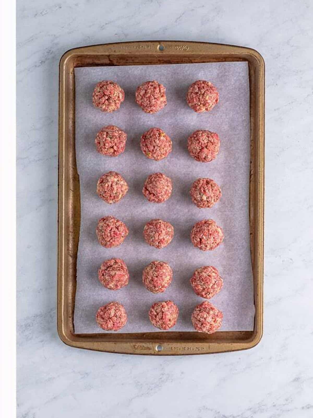 Rolled raw meatballs on a parchment-lined baking tray.