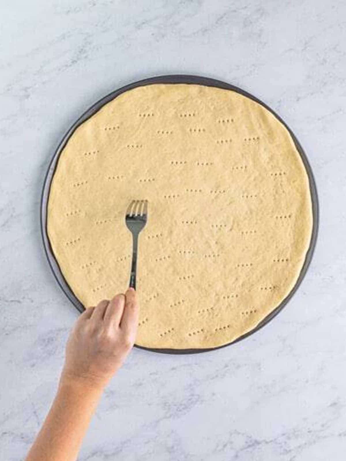 Stretching pizza dough on a pan and piercing it with a fork.