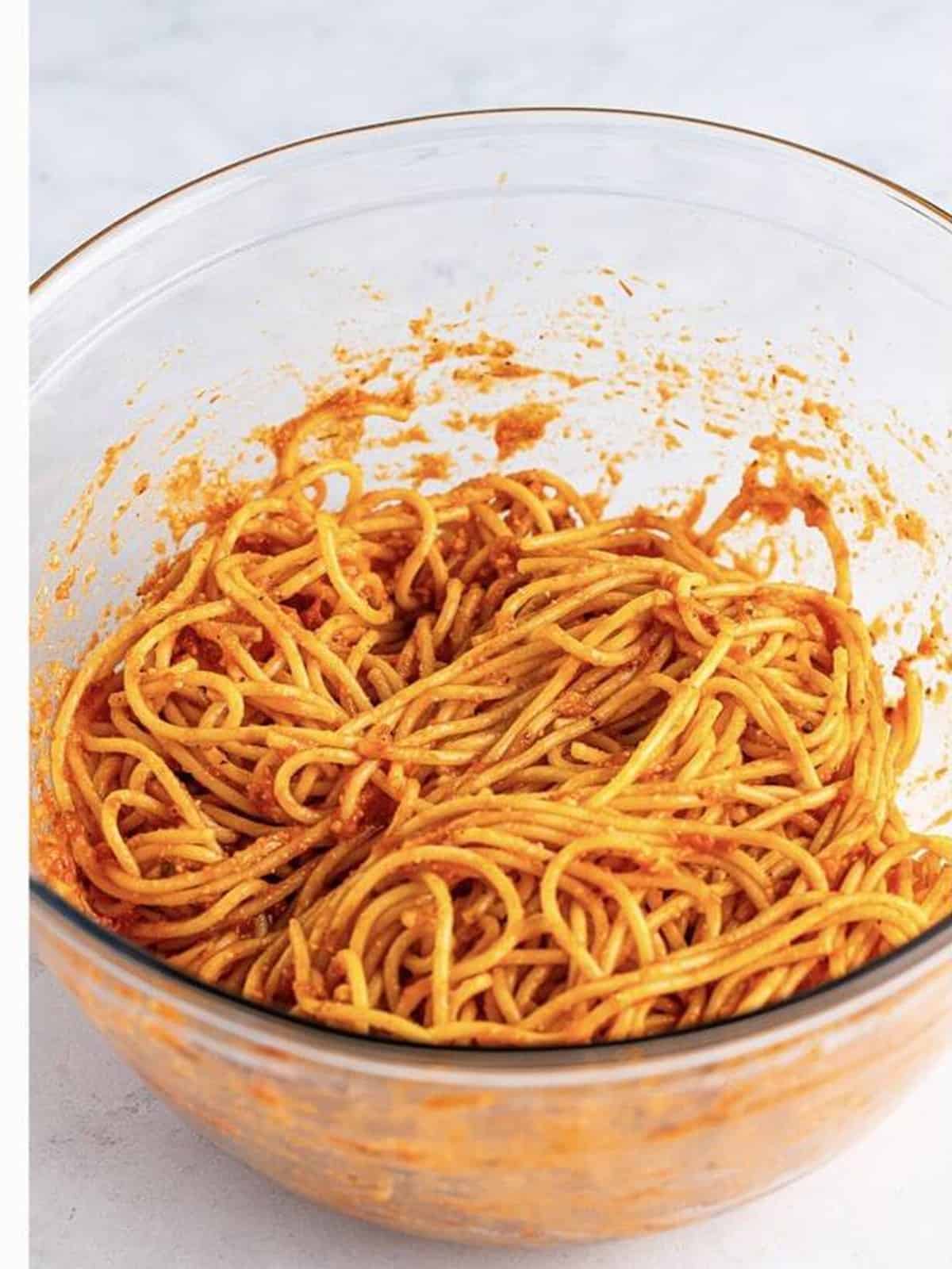 Cooked spaghetti tossed with marinara and parmesan in a glass bowl.