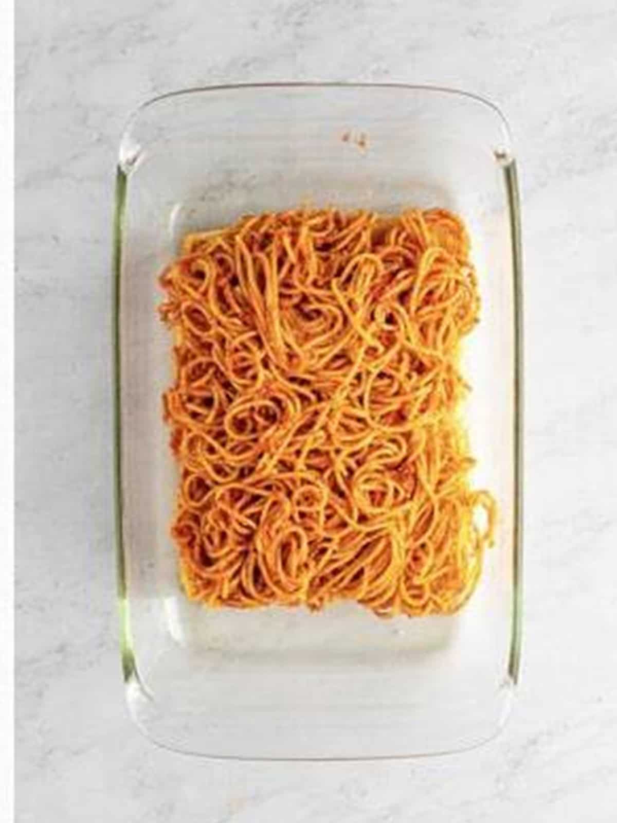Saucy spaghetti layered over Hawaiian roll bottoms in a baking dish.