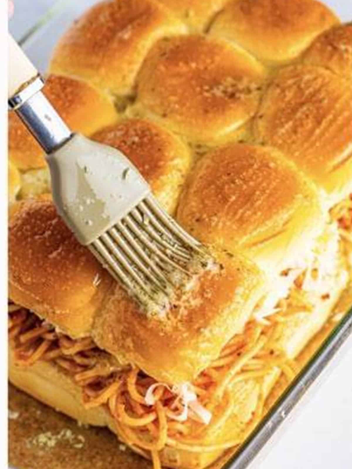 Brushing garlic butter over the tops of the Hawaiian roll sliders.