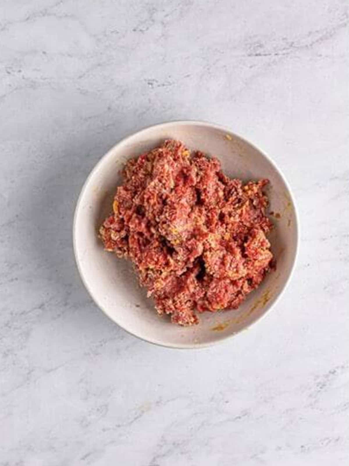 Ground beef, parmesan, panko, and seasonings mixed together for meatballs in a bowl.