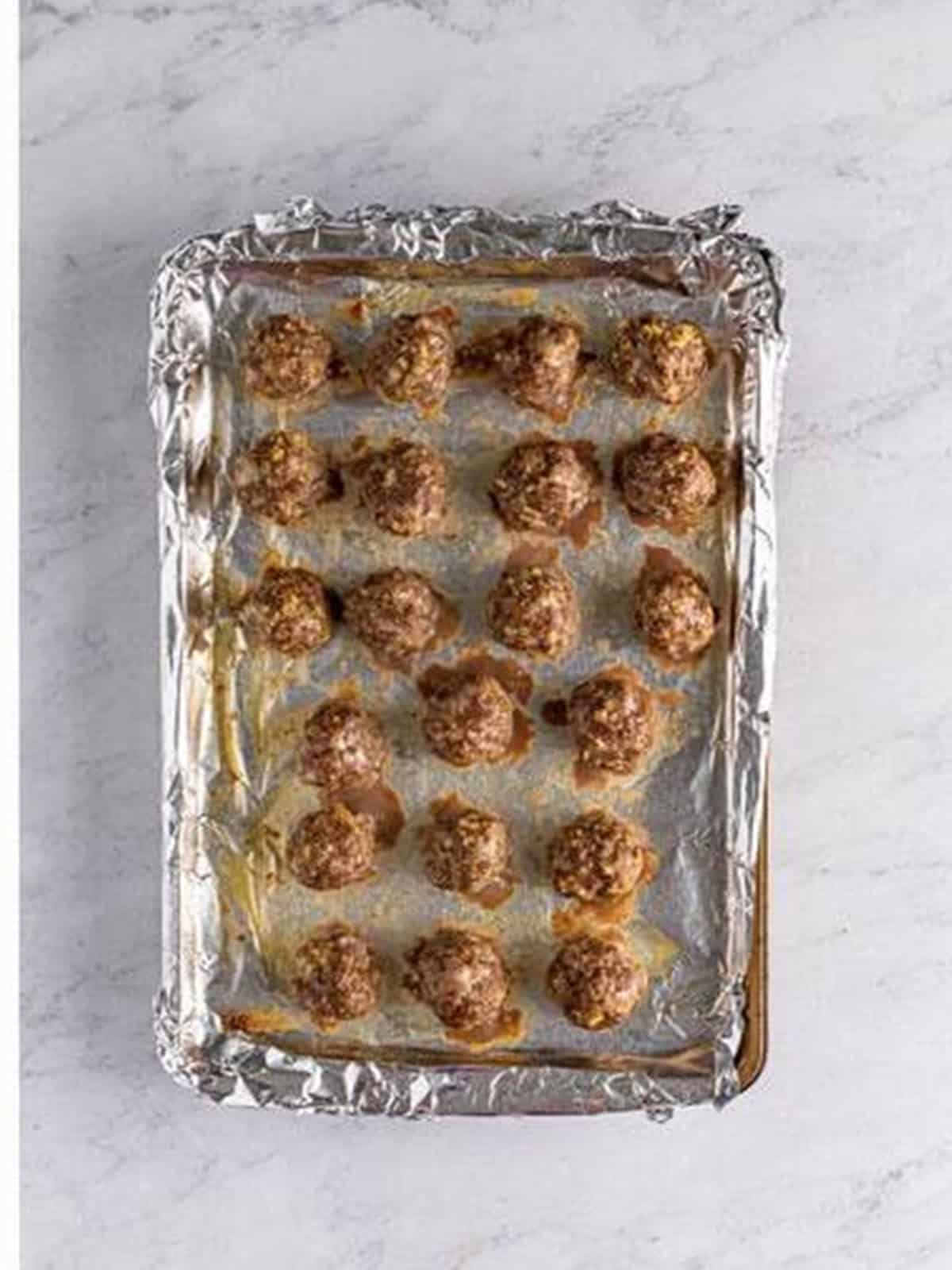 Baked golden meatballs on a parchment lined baking sheet.