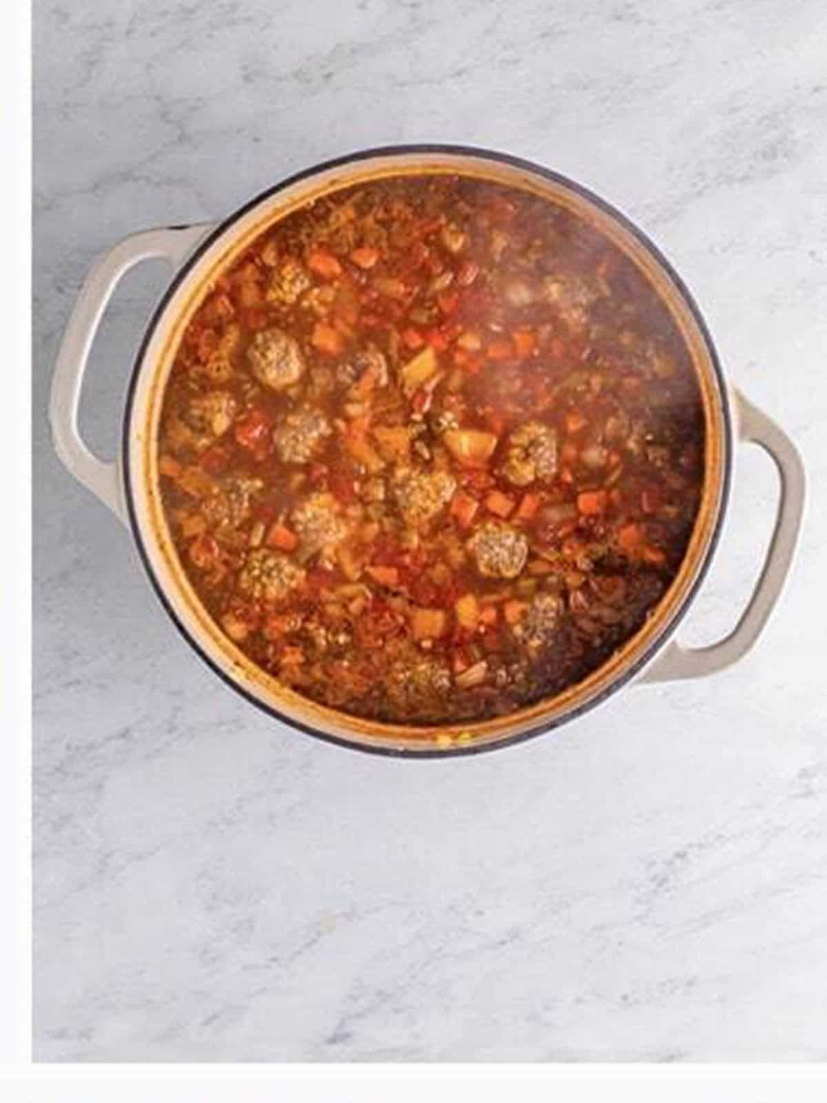 Italian meatball soup simmering with meatballs in a pot.