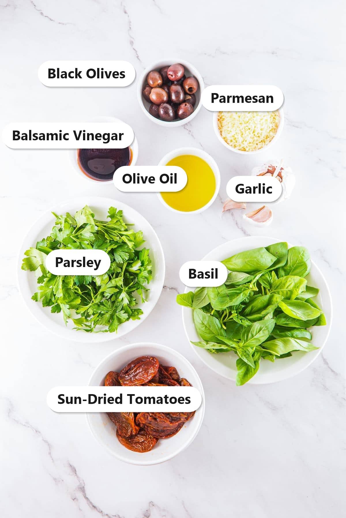 Labeled ingredients for Mediterranean dip including sun-dried tomatoes, olives, parmesan, basil, parsley, garlic, and olive oil.