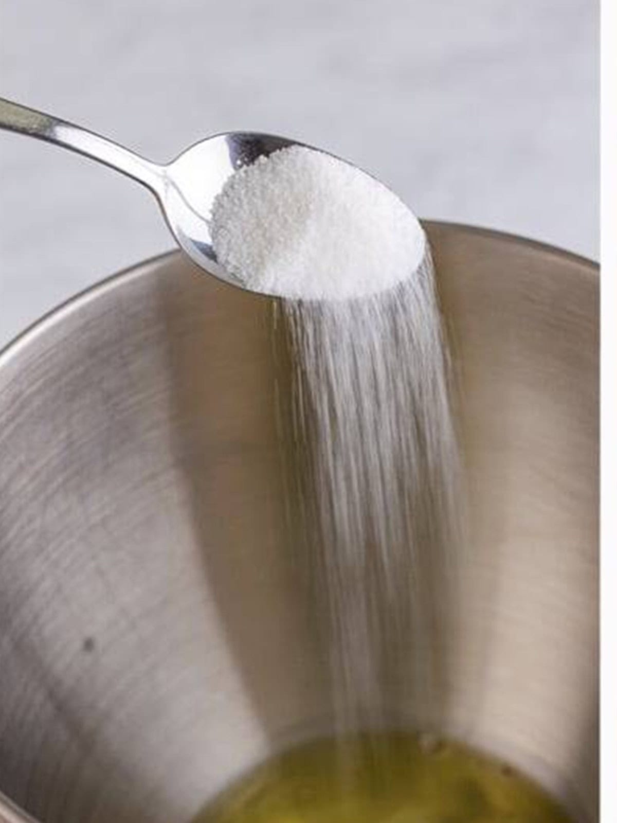Granulated sugar being poured into whipping egg whites in a stand mixer for meringue cookies.