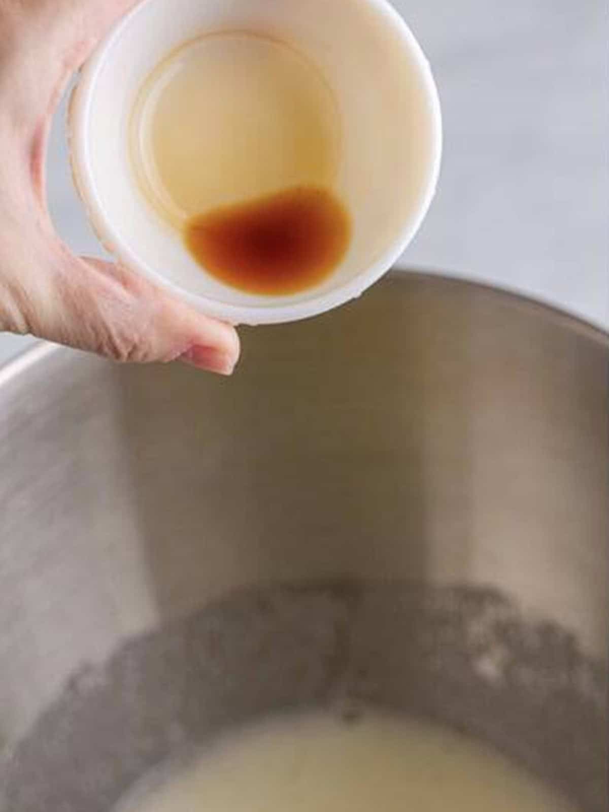 Vanilla extract being added to the meringue mixture in a stand mixer.
