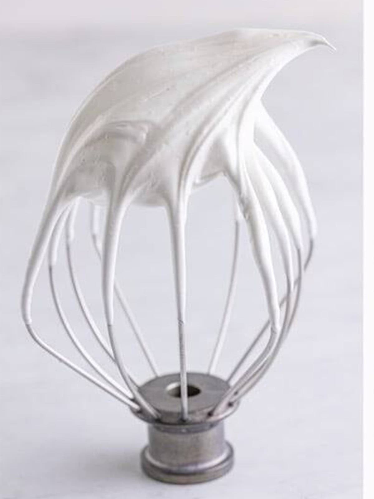 Glossy stiff peaks of meringue on a stand mixer whisk attachment.