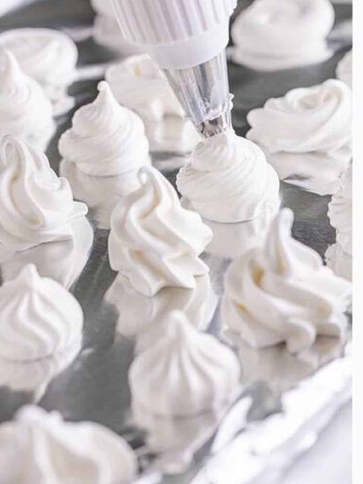 Meringue piped into swirled cookie shapes on a lined baking sheet.