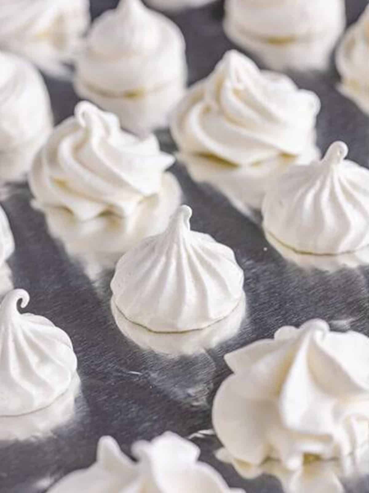 Baked vanilla meringue cookies cooling on a baking sheet.