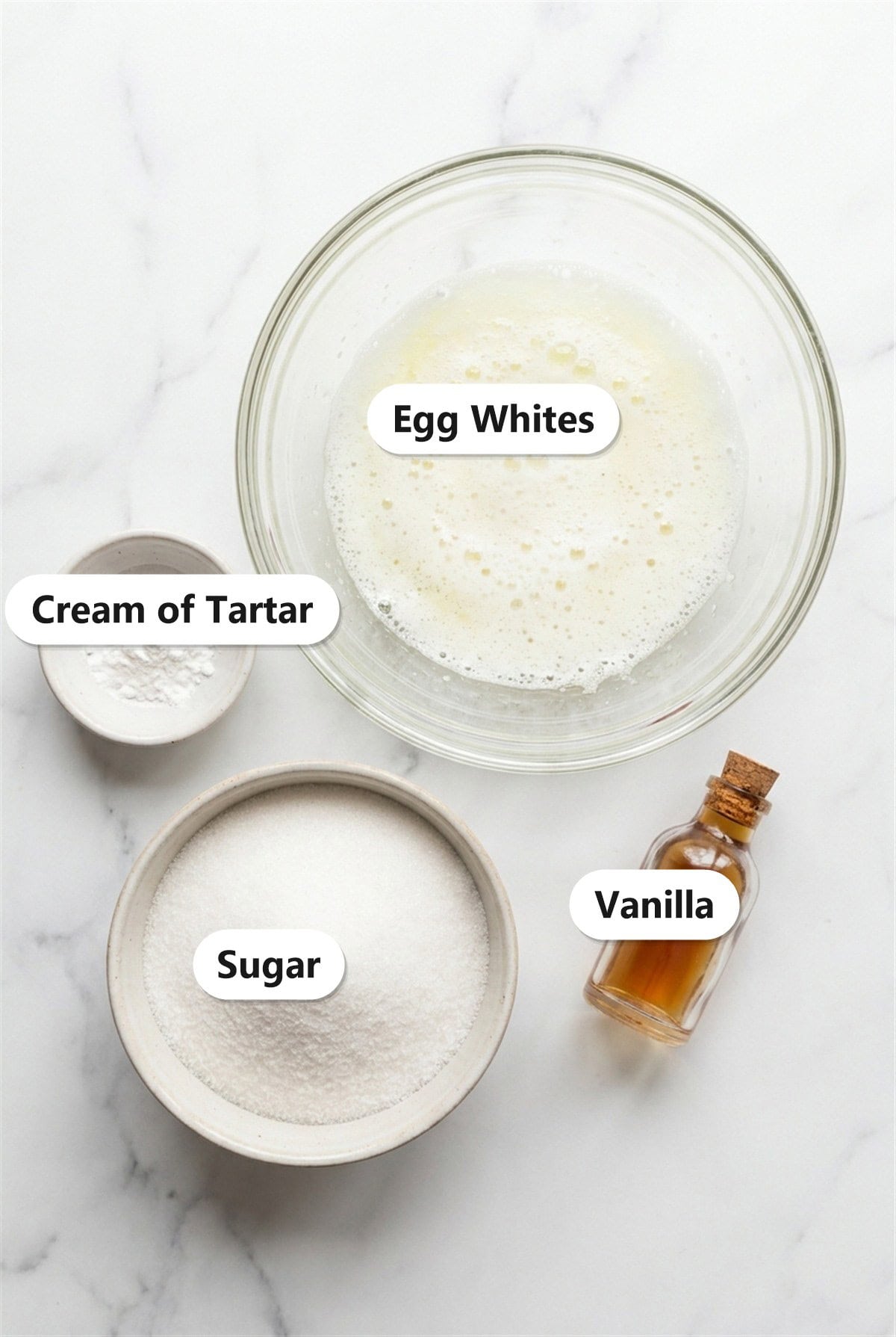 Meringue Cookies ingredients including egg whites, granulated sugar, cream of tartar, and vanilla labeled on a marble surface.