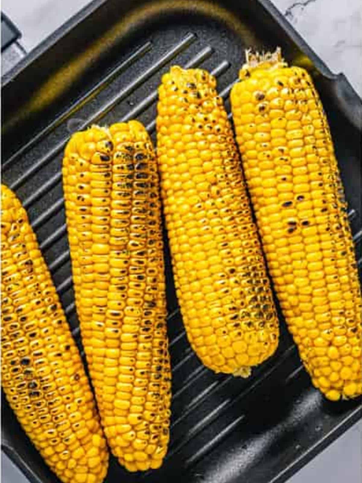Ears of corn on a grill pan starting to char.