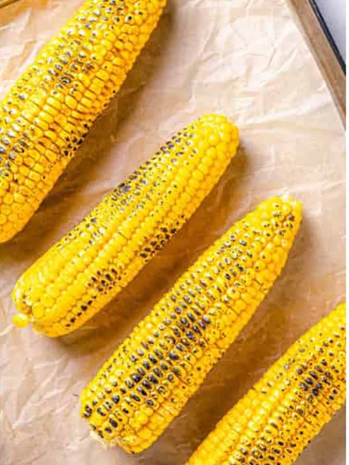 Charred grilled corn on the cob resting on parchment paper.