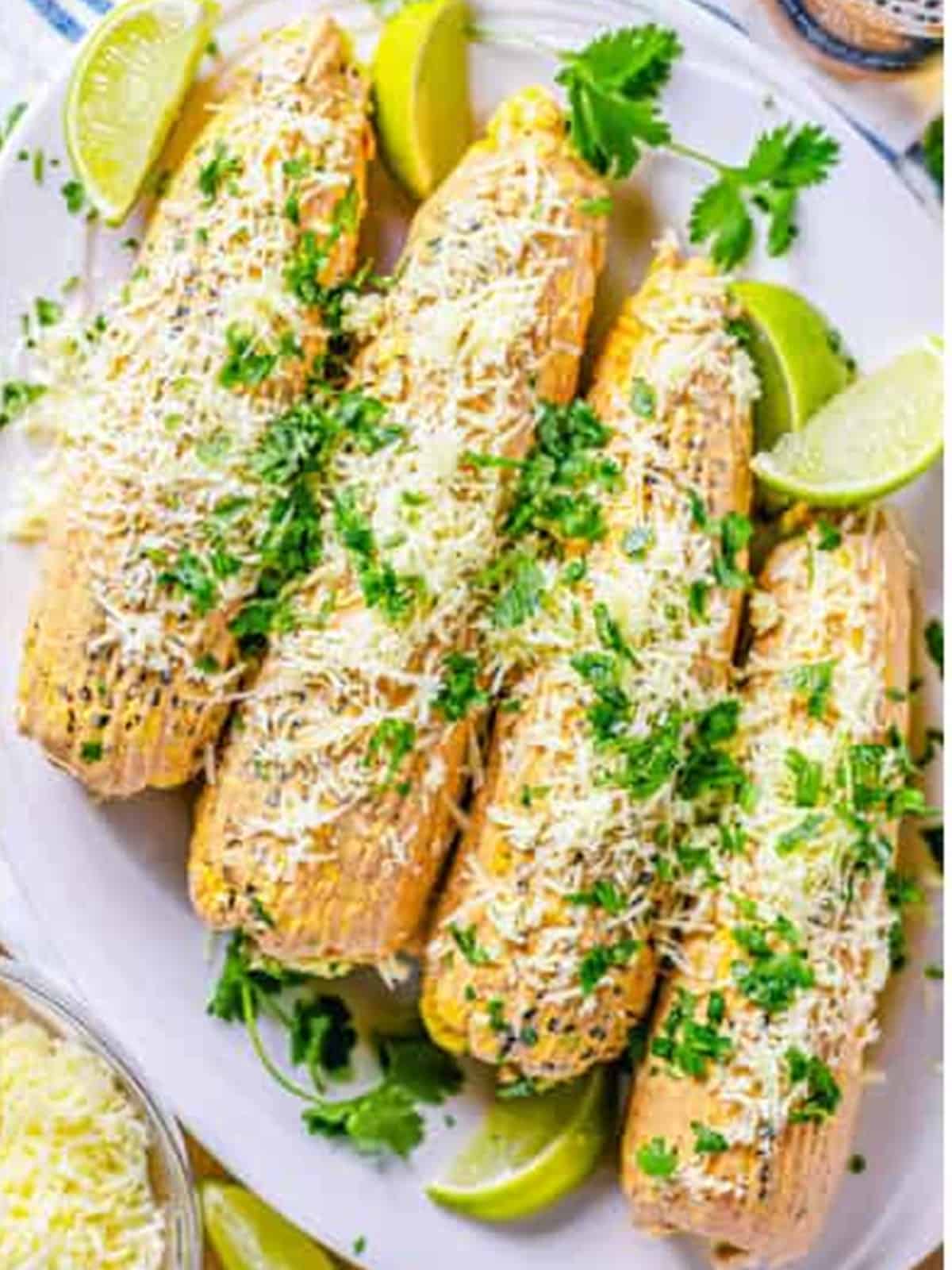 Finished Mexican street corn topped with white cheddar, cilantro, and lime on a platter.