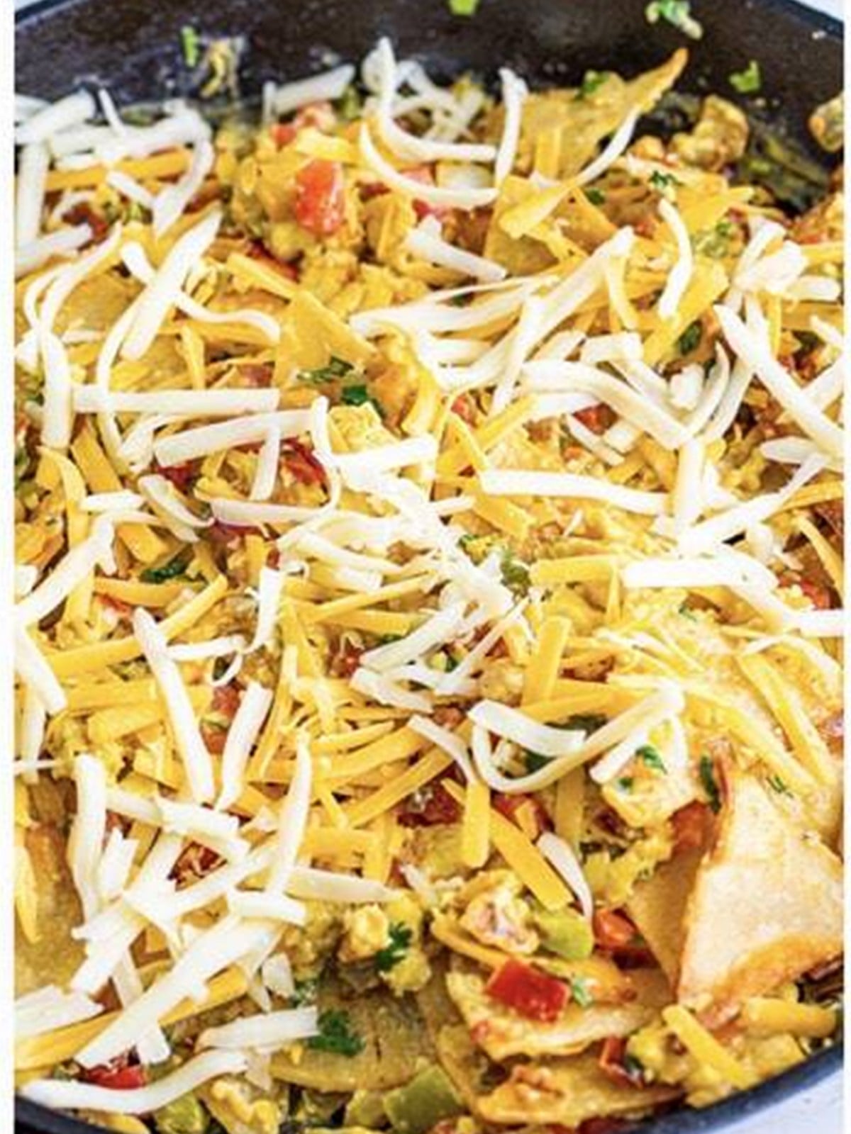 Migas topped with melted cheese and crispy tortilla strips in a cast iron skillet.