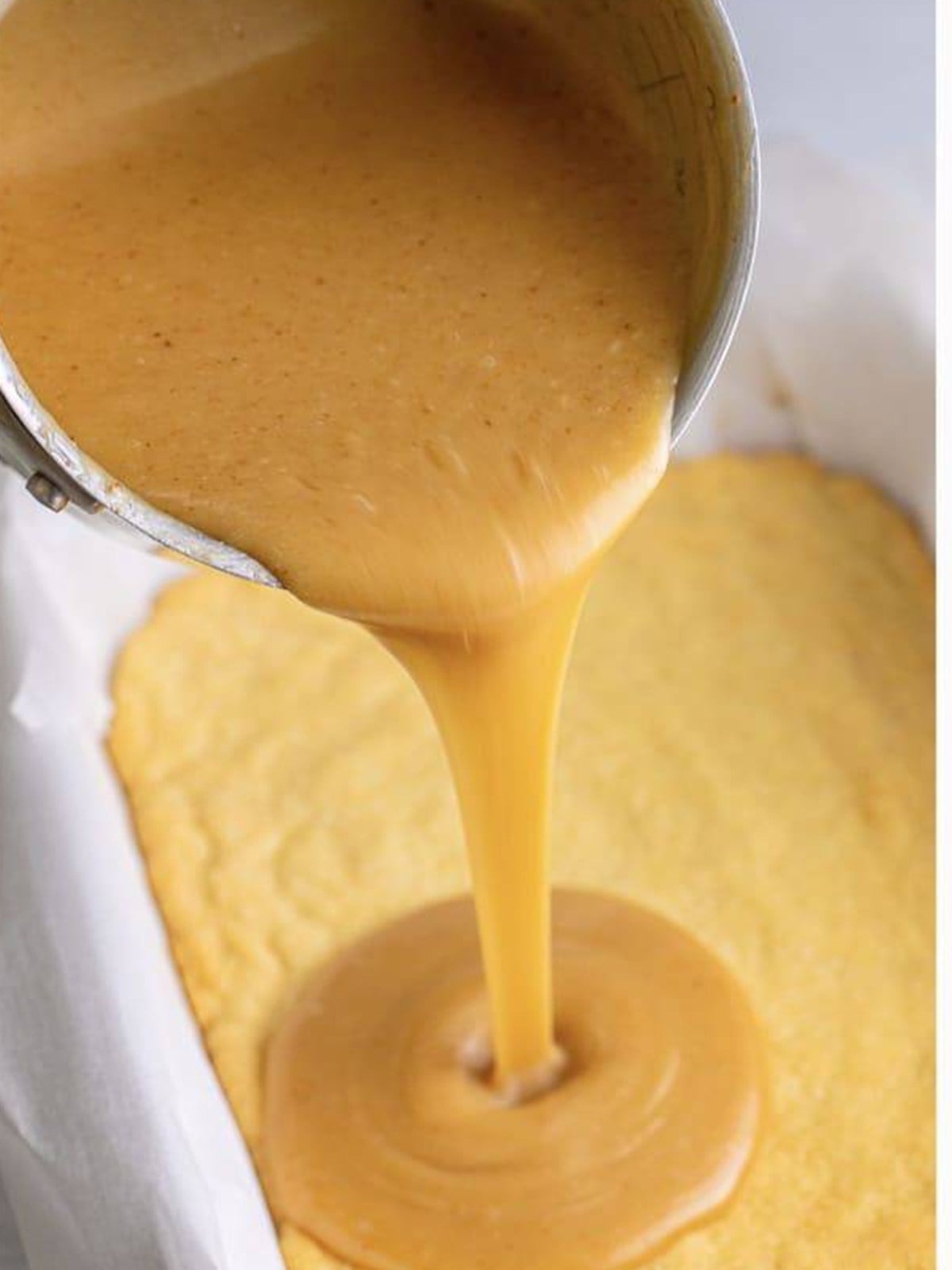 Pouring caramel over the baked shortbread layer for millionaires shortbread.