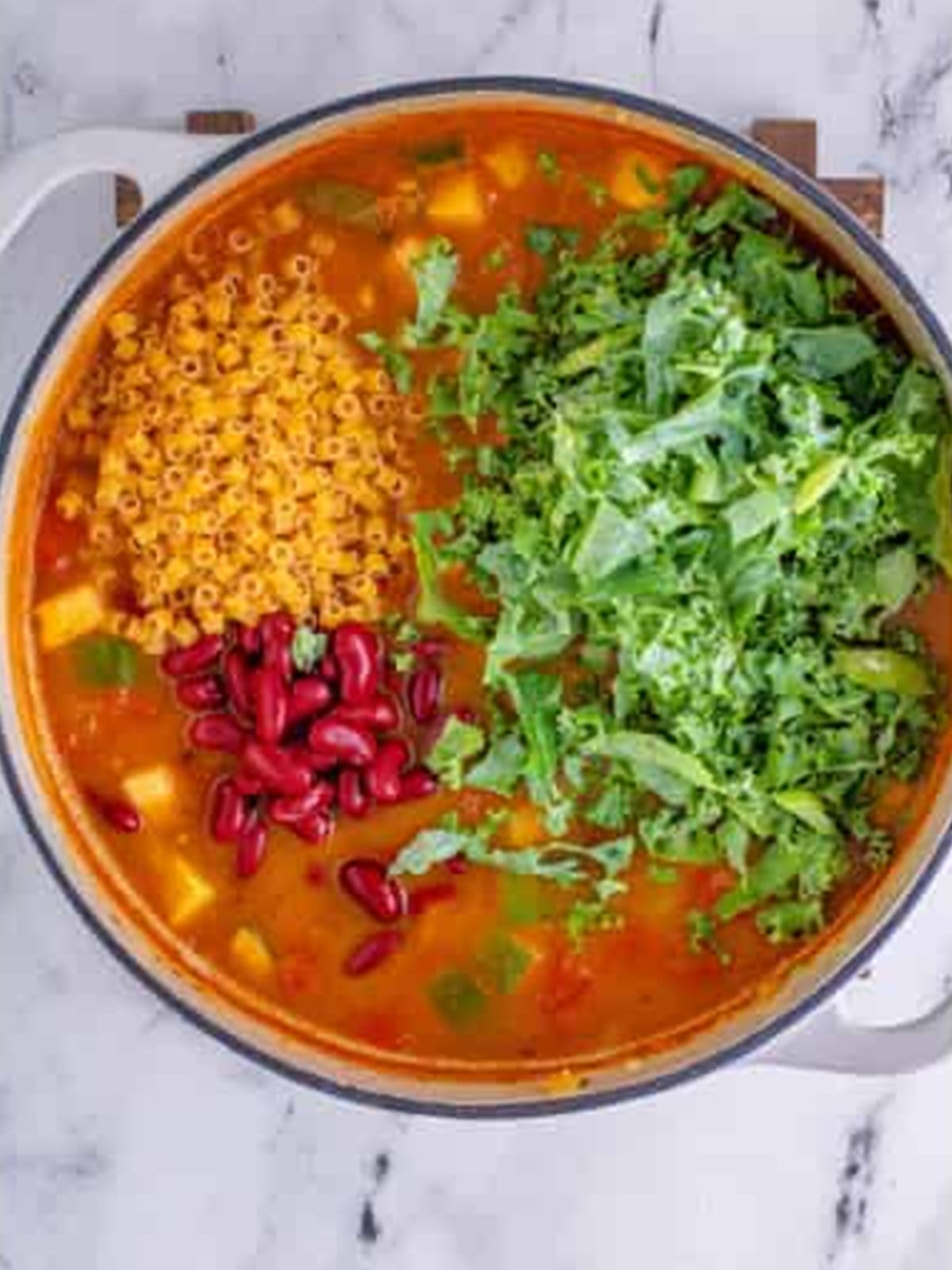 Pasta, kidney beans, and kale added to simmering minestrone soup.