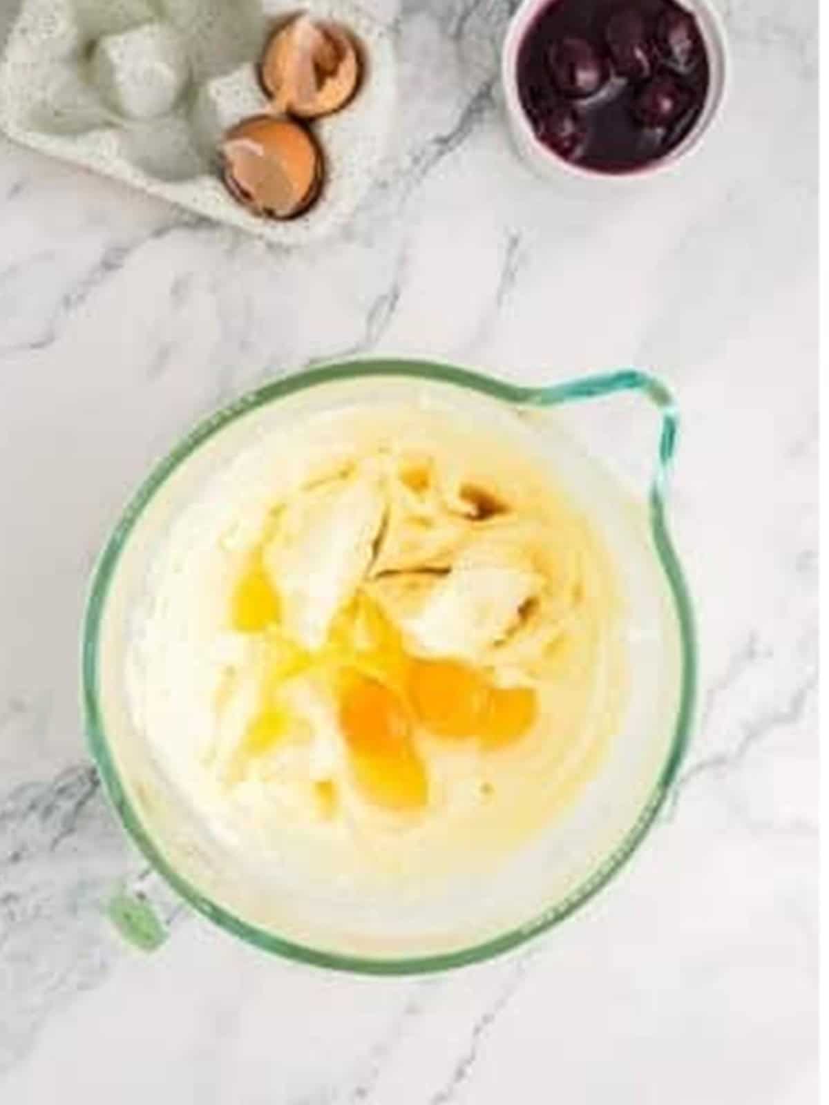 Adding eggs and vanilla to the cheesecake filling.