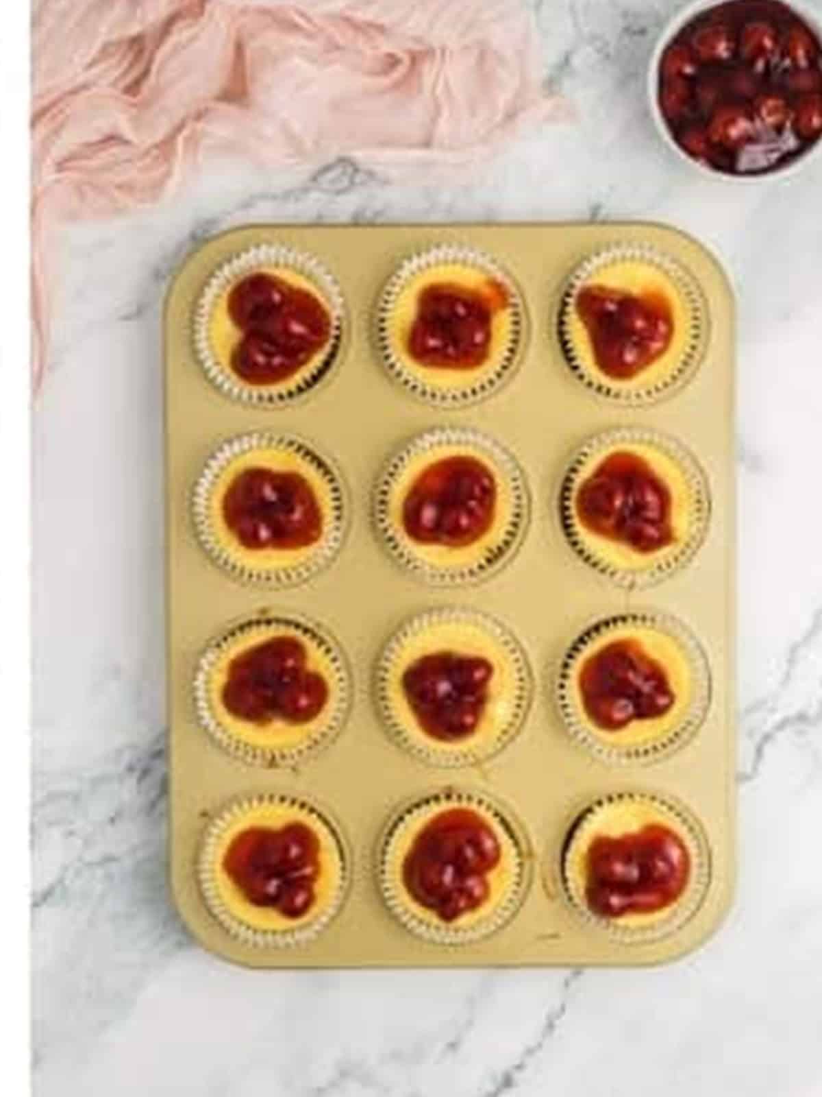 Mini cheesecakes topped with cherry pie filling in the muffin tin.