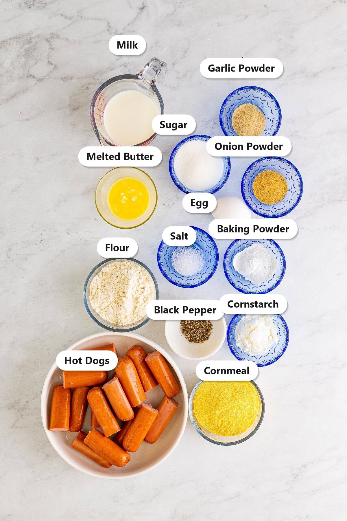 Labeled ingredients for homemade mini corn dogs including hot dogs, cornmeal, flour, milk, egg, butter, sugar, and spices.