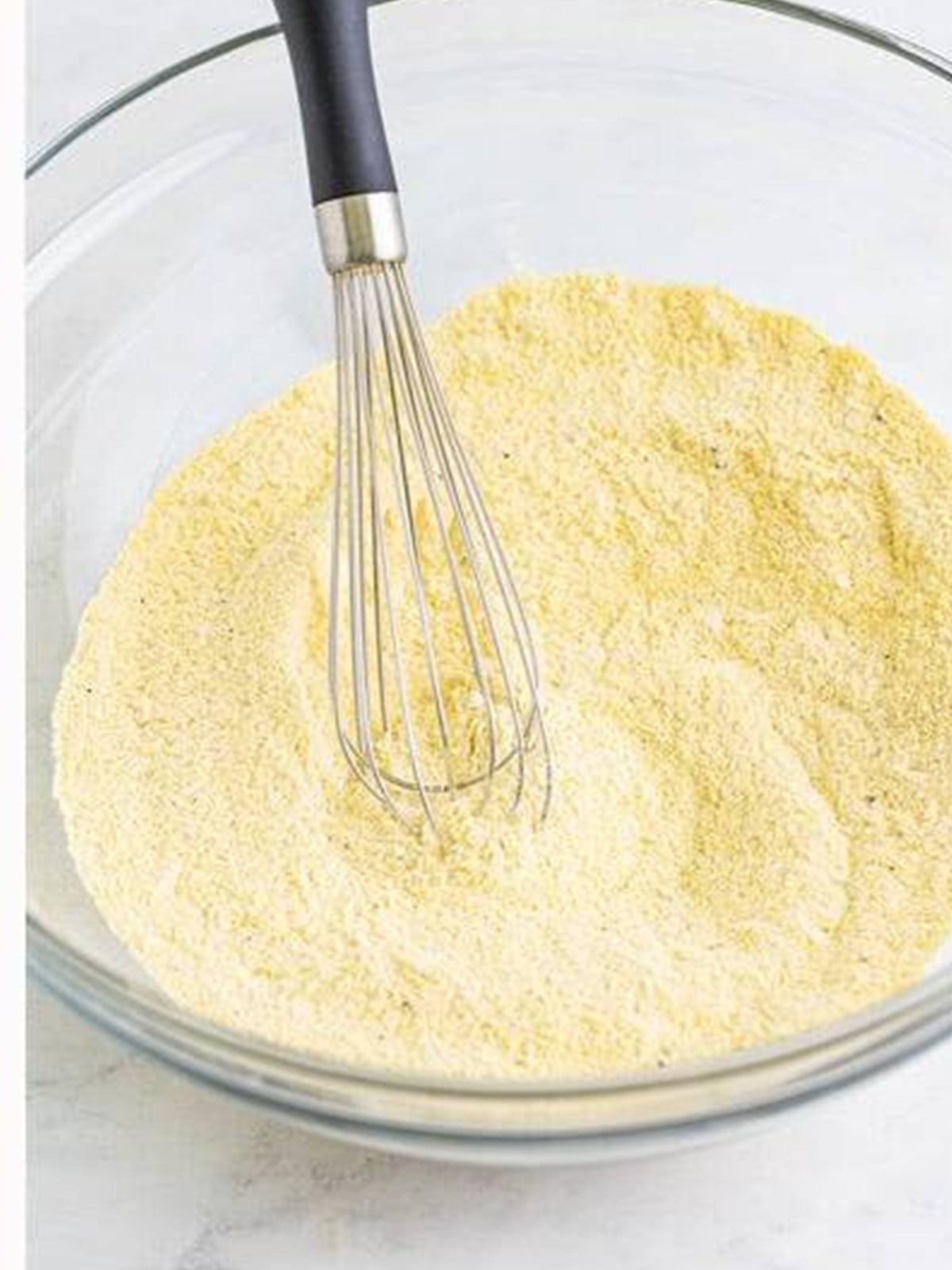 Cornmeal, flour, sugar, and spices whisked together in a glass bowl.