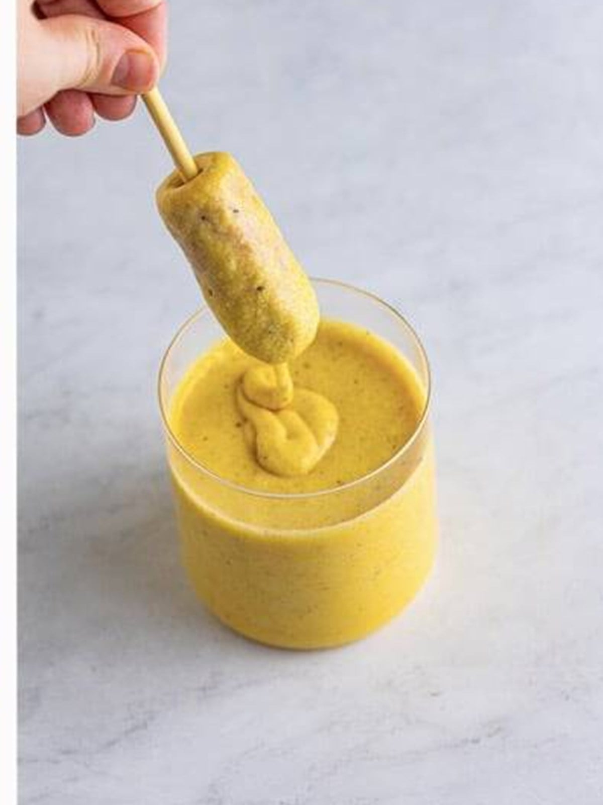 A skewered hot dog dipped into the cornmeal batter until fully coated.