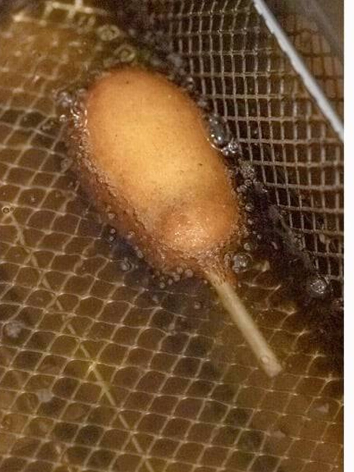 Battered mini corn dogs frying to golden brown in hot oil.